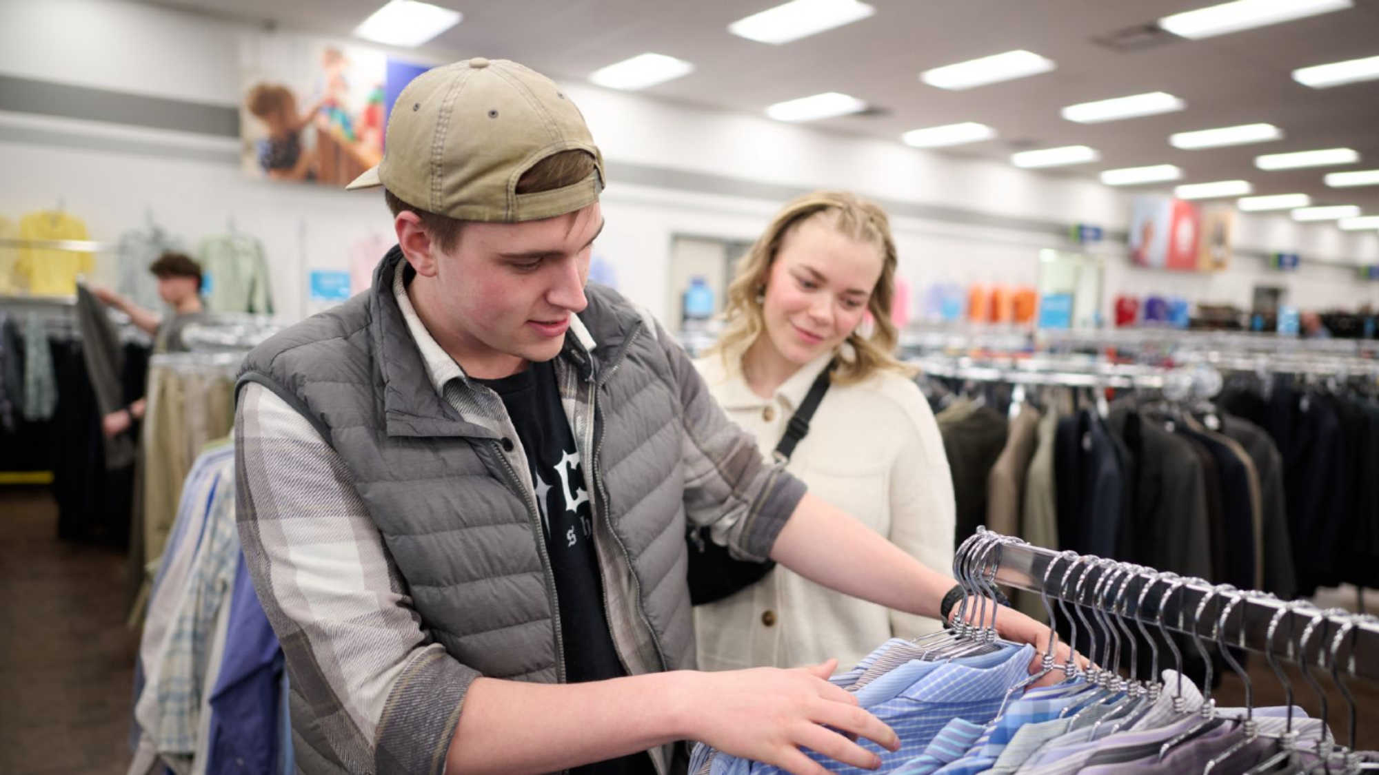 A young man and a young woman browsing the clothing racks at their local DI